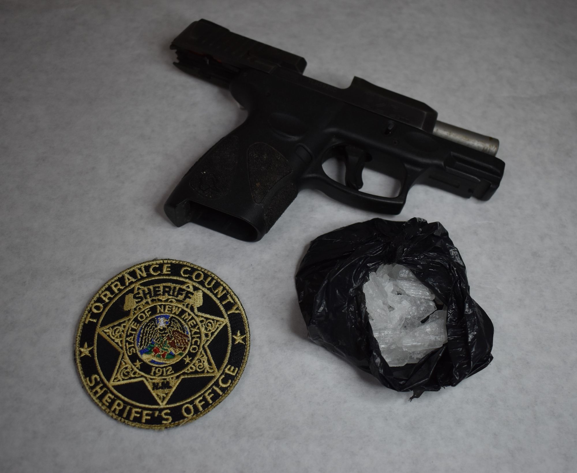 Photo of a Taurus G2c 9mm Handgun, a black plastic bag containing crystal meth, and a patch for the Torrance County Sheriff's Office.