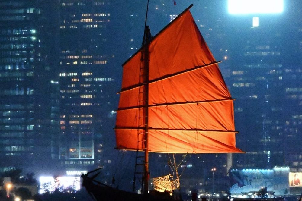 color street photography of red junk boat sailing in Victoria Harbour of Hong Kong at night