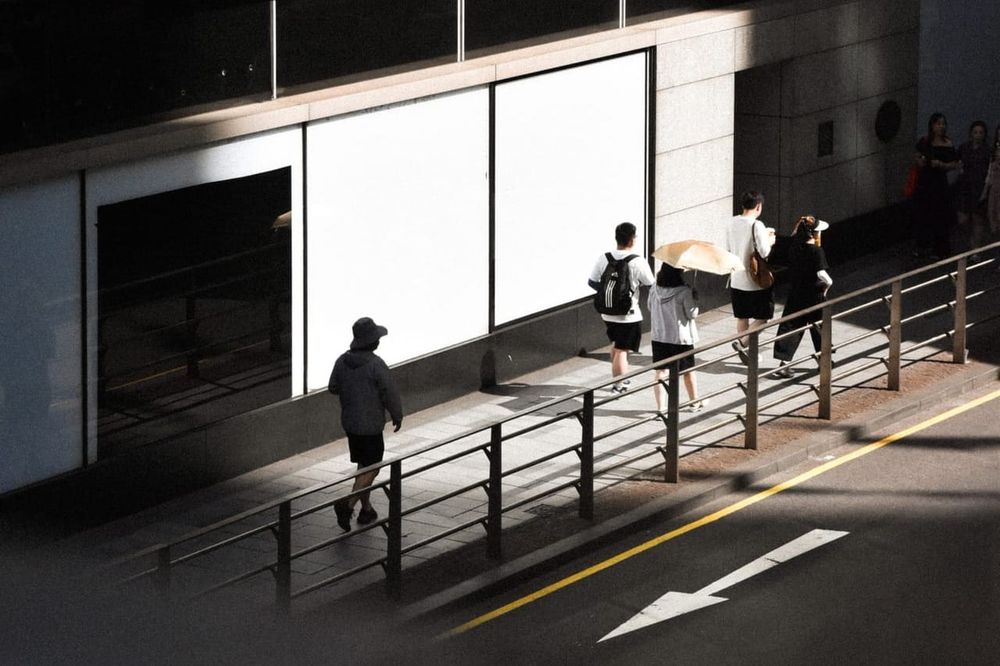 color street photography of people walking past a building with light and shadow on it