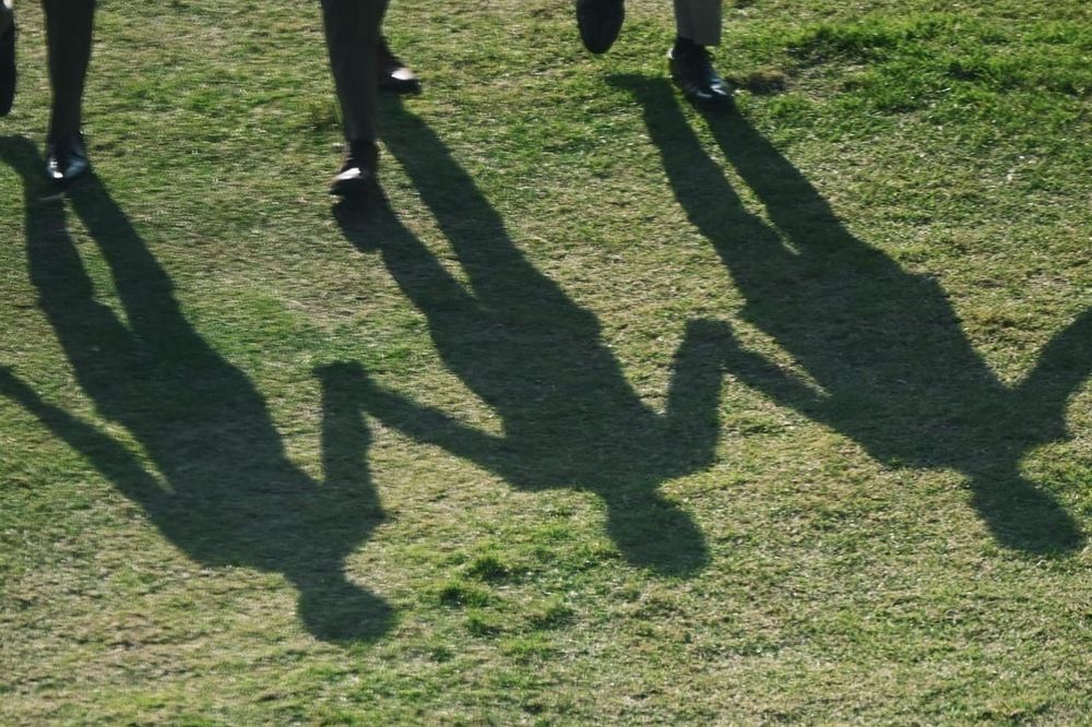 color street photography of shadows of men holding hands on lawn