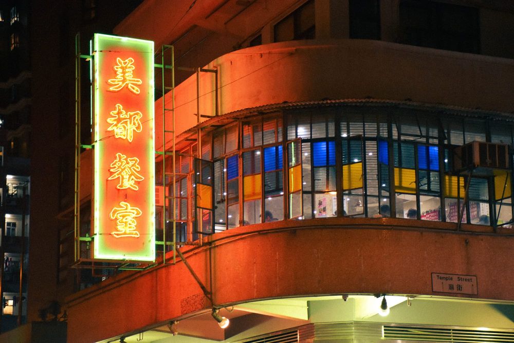color street photography of a glowing red neon sign of hong kong style diner adhered to tong lau at night