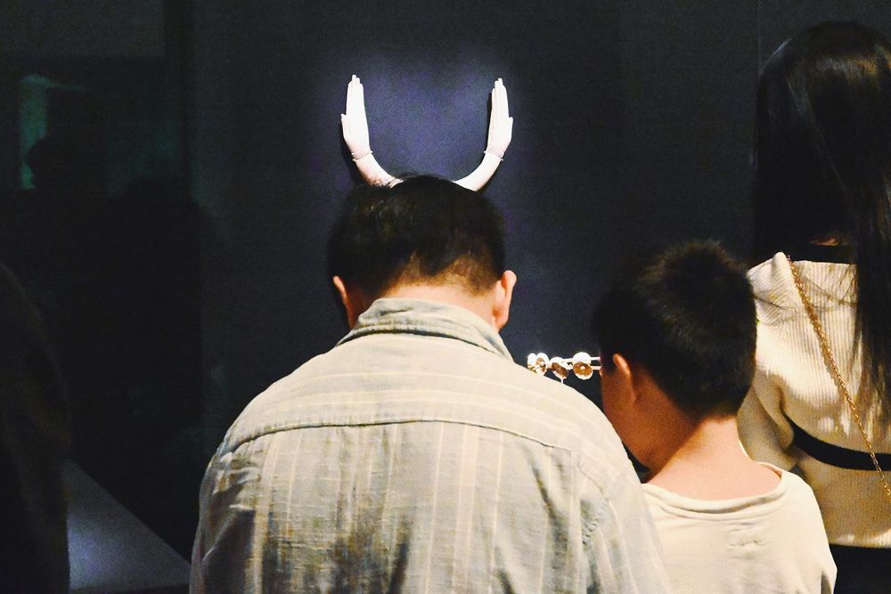 color street photograpy of a pair of hand-shaped artifacts juxtaposing with the head of a visitor in museum