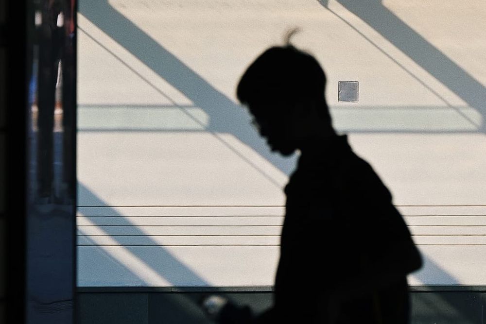 color street photography of a silhouette of a person in front of a building with lights and shadows on it 