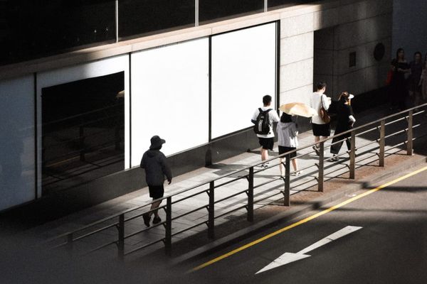 color street photography of people walking past a building with light and shadow on it