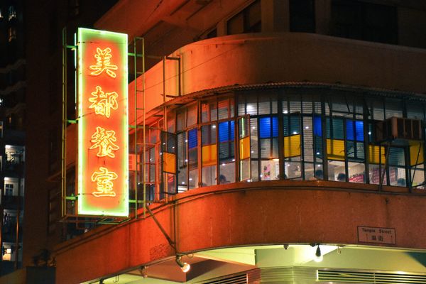 color street photography of a glowing red neon sign of hong kong style diner adhered to tong lau at night