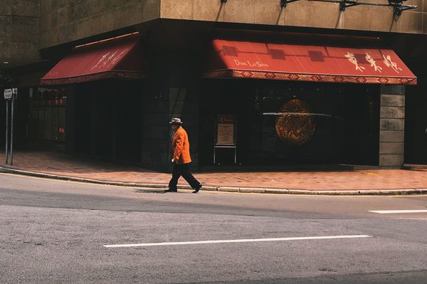 color street photography of man in orange blazer and a hat walking past a Chinese restaurant with red awnings