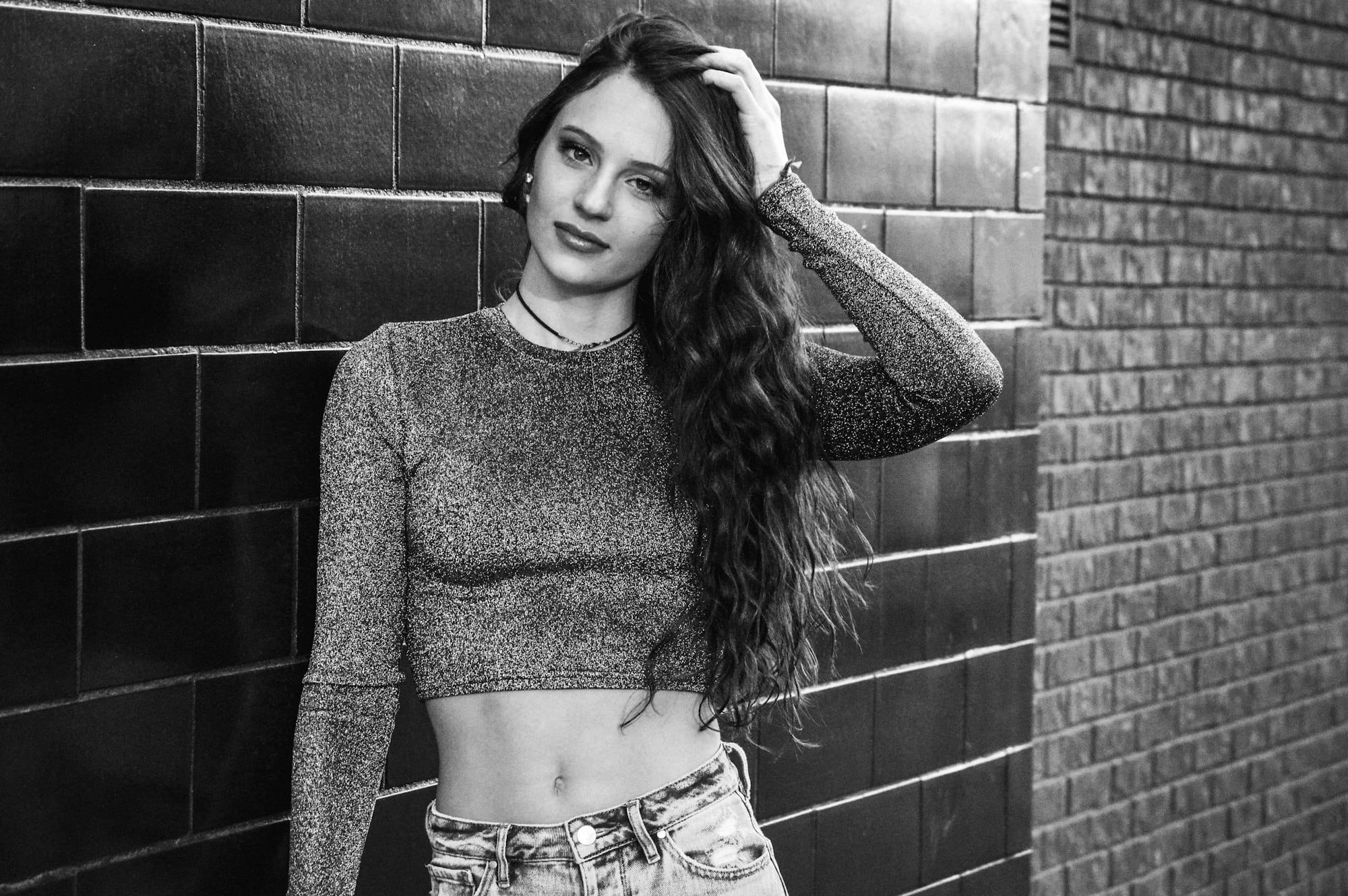 woman in gray sweater standing beside brick wall