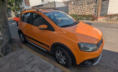 A bright orange four-door Volkswagen hatchback, parked at the curb under a tree.