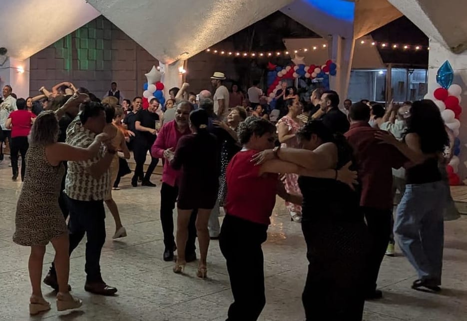 partners smiling on a dance floor, with red white and blue balloons around them.