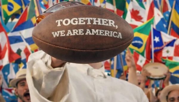 A screenshot of Bad Bunny from his Super Bowl performance. His face is hidden by a football with the words "Together, we are America." The flags of various nations are behind him.