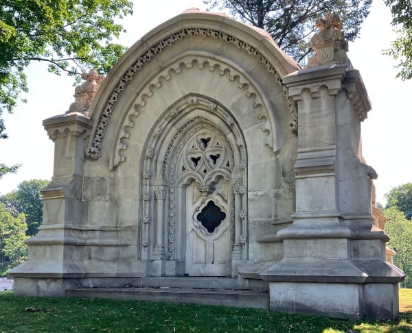 an elaborate mausoleum with gothic details. at the corners are statuary bearing the letter "M"