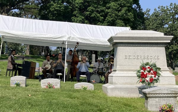 white tent with a jazz combo underneath. In front of it is a large monument bearing the name "Beiderbecke"