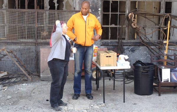 a woman with red hair scratching her head, next to a taller person looking at her intently. standing outside next to stacks of theater stuff