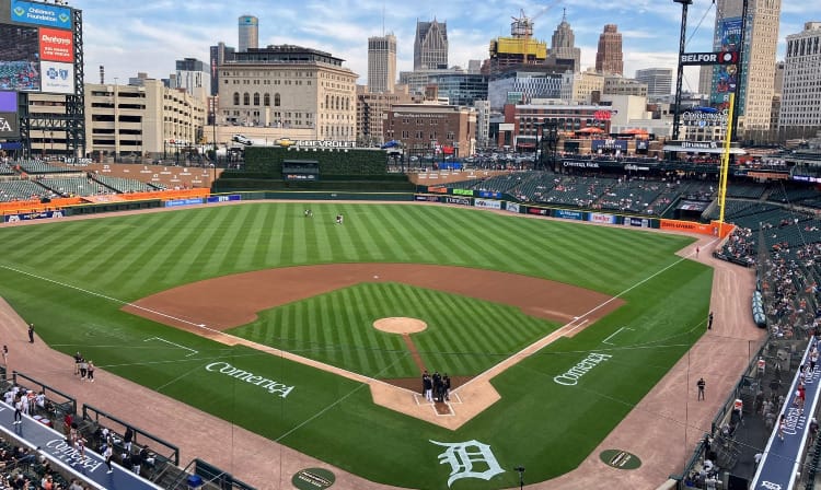 Umpires meeting with managers at home plate in Comerica Park in Detroit. The buildings of downtown are beyond the outfield stands.