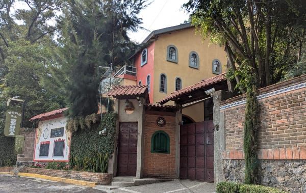 The exterior of Cultural Center Foro la Negra. It is a large, ochre and salmon house behind a tall brick wall with a gate covered by a tile roof.