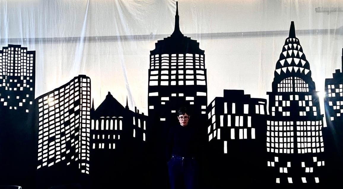 A person standing in front of a black silhouette of buildings

Description automatically generated