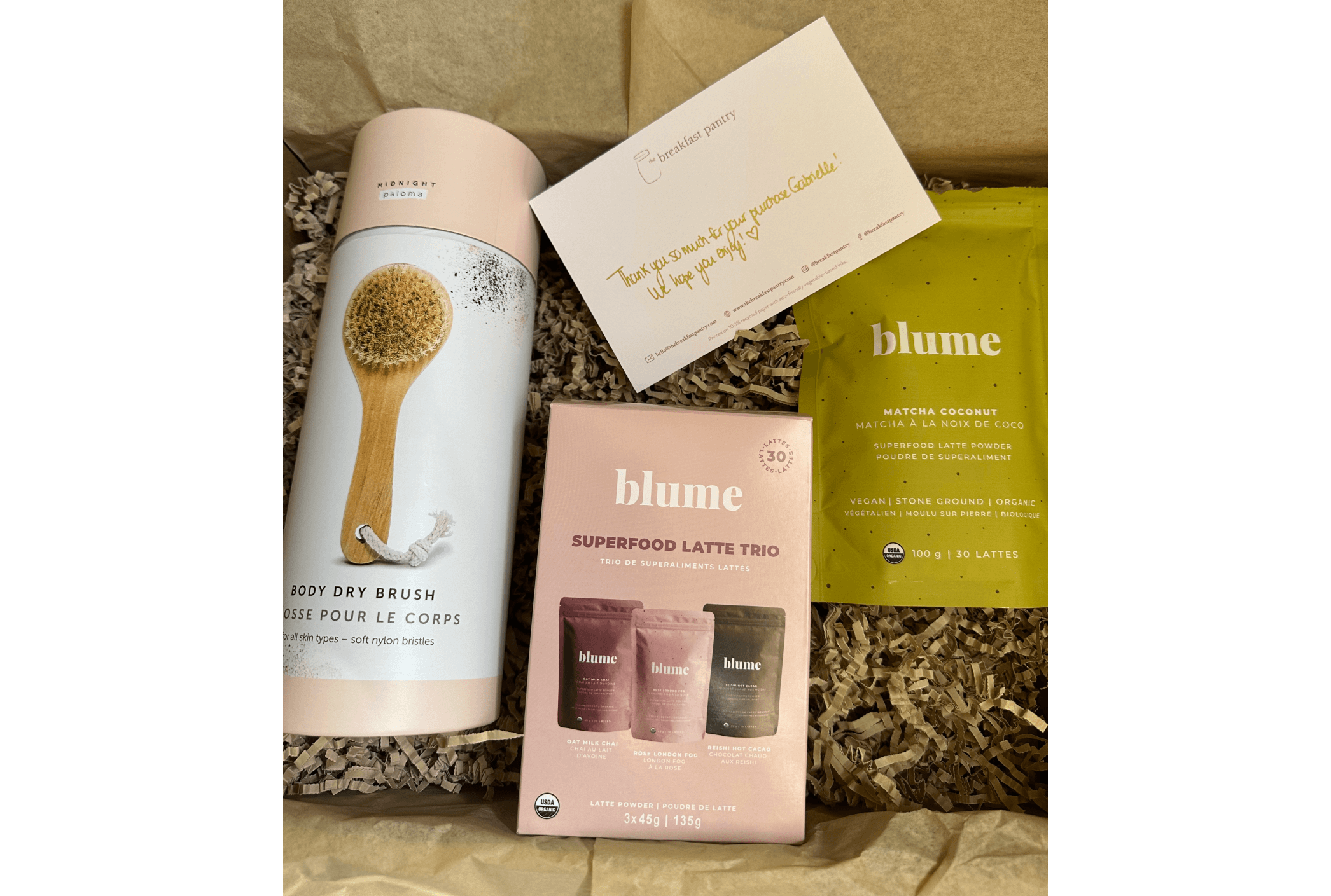 An image of an order from The Breakfast Pantry showing the products in a box with brown crinkle paper and a handwritten thank you note.