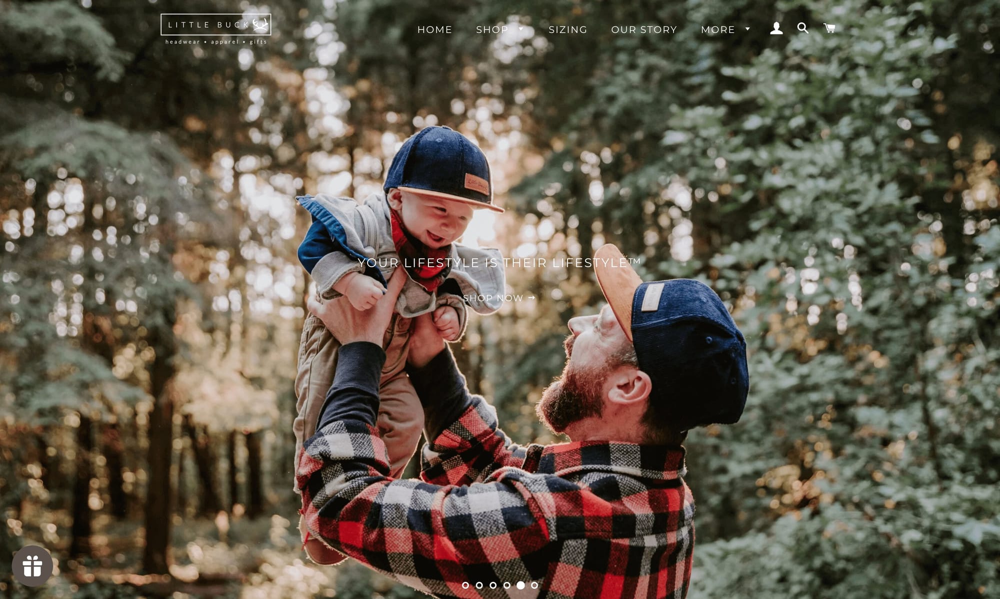 A screenshot of Little Buck’s homepage showing a dad holding his baby in matching snapback navy blue Little Buck hats.&nbsp;