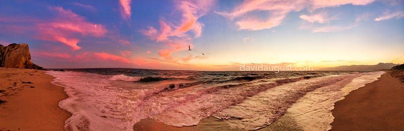 coloruful dusk on an ocean beach as waves cover some of the sand and pink and white cliuds are in the sky above the beach and cliffs