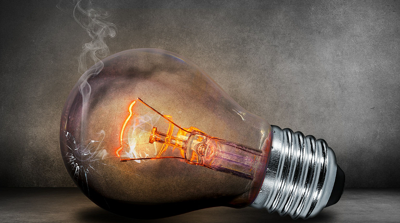 incandescent lightbulb laying on its side, filament glowing, bulb cracked and smoke rising from the crack
