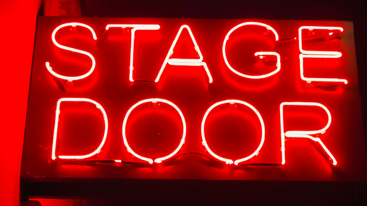 A bright red neon sign with white glowing letters that reads "STAGE DOOR."