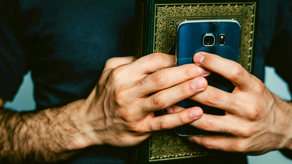 Hands holding a smartphone with the camera open, positioned next to an ornate book with a decorative cover.