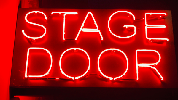 A bright red neon sign with white glowing letters that reads "STAGE DOOR."