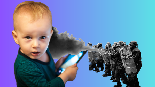A toddler in a green shirt holds a cell phone as a line of riot police fires chemical agents at them.