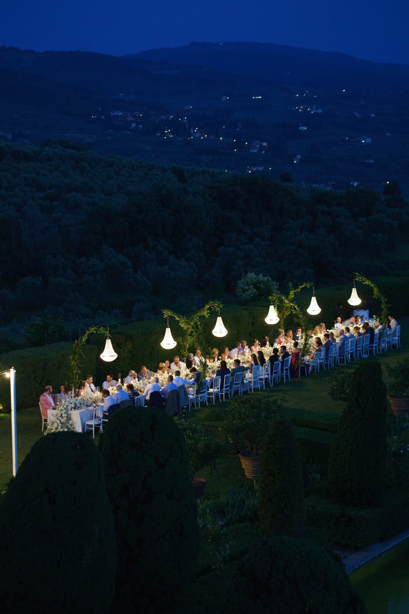 Aerial view of a long dinner table lit on a hillside at dusk