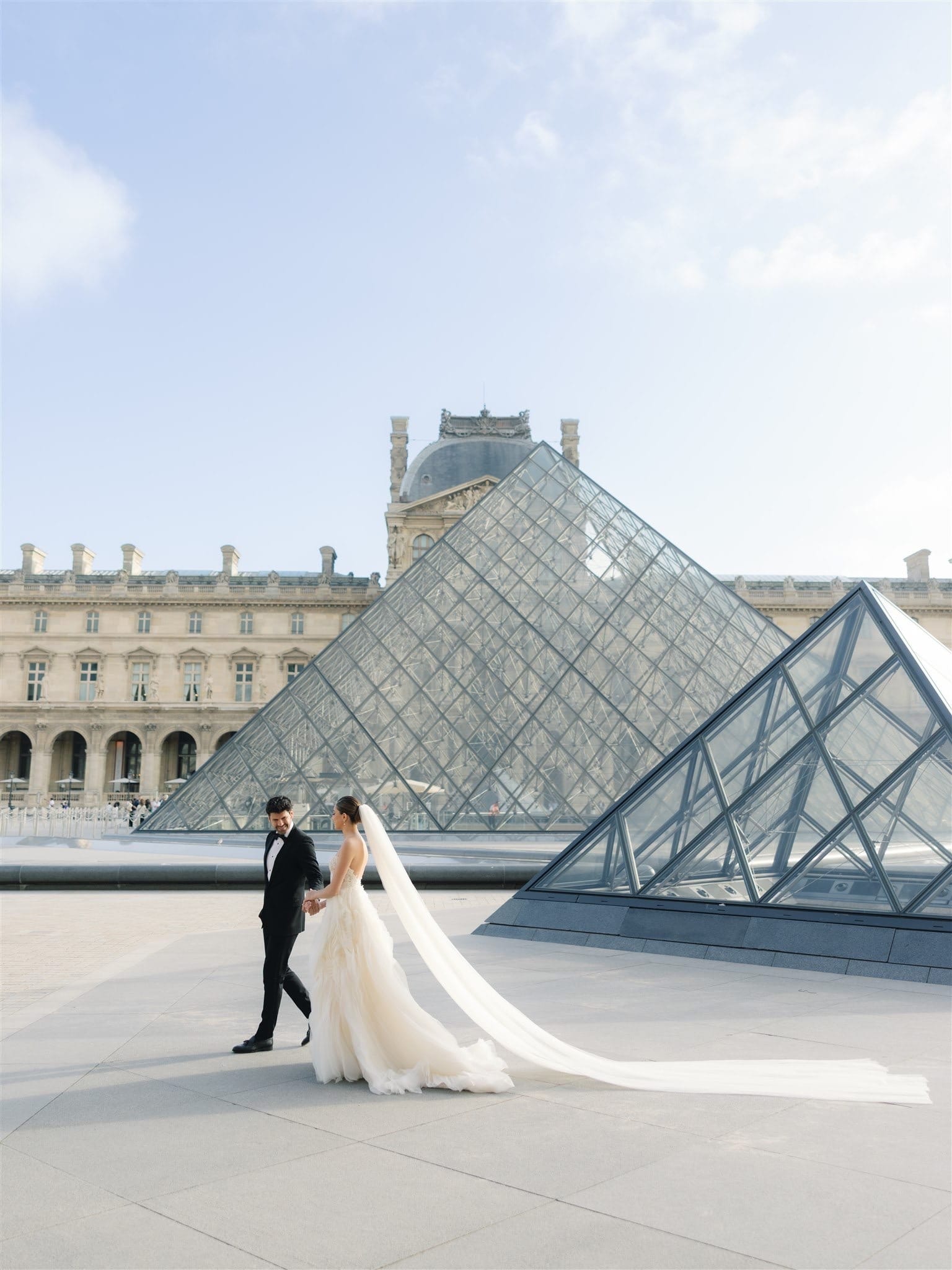 A couple walking hand in hand past the Louvre pyramid in Paris