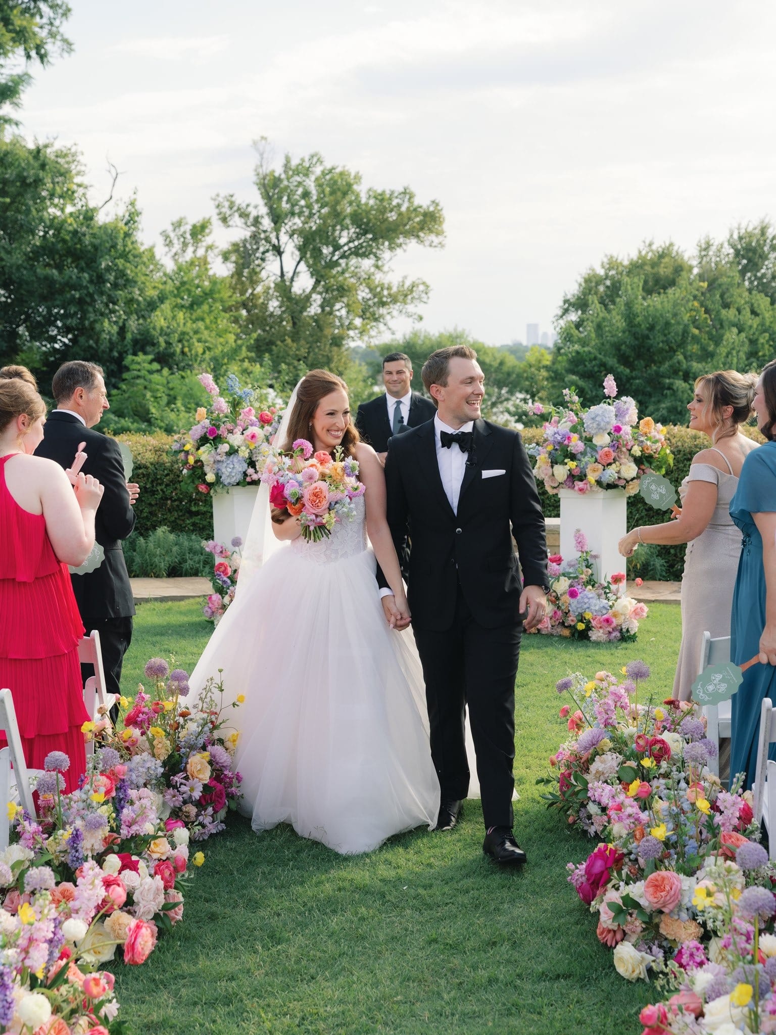 A couple walking up a garden aisle lined with colorful florals