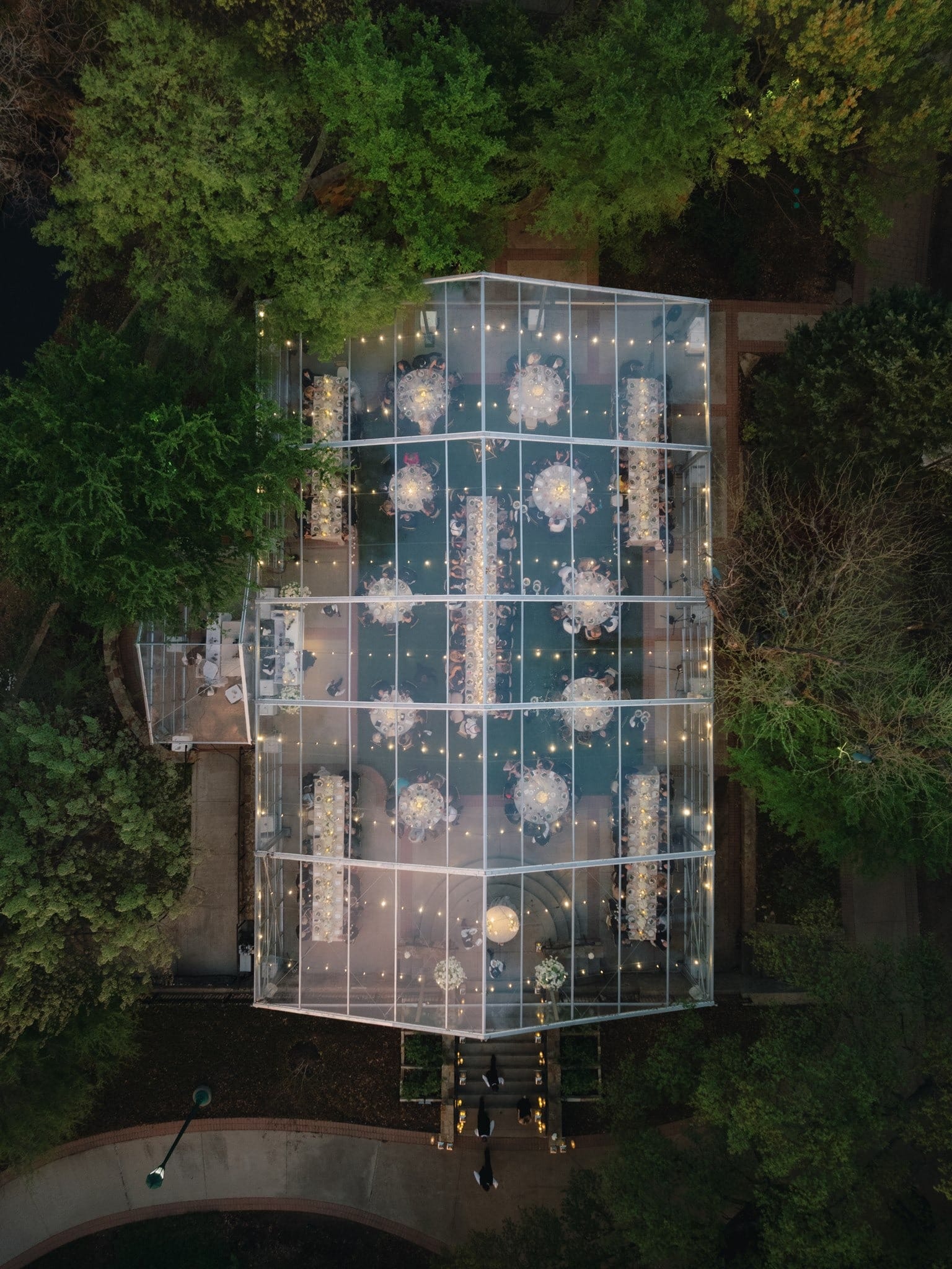 Aerial view of a clear tent lit up at night among trees