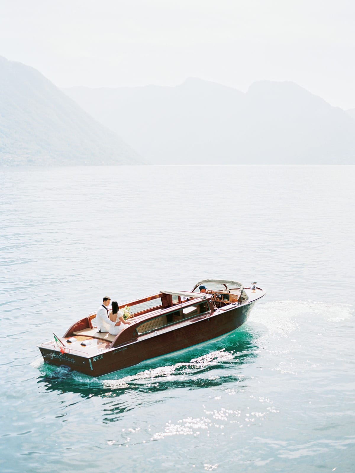 A wooden boat crossing a calm lake with mountains behind