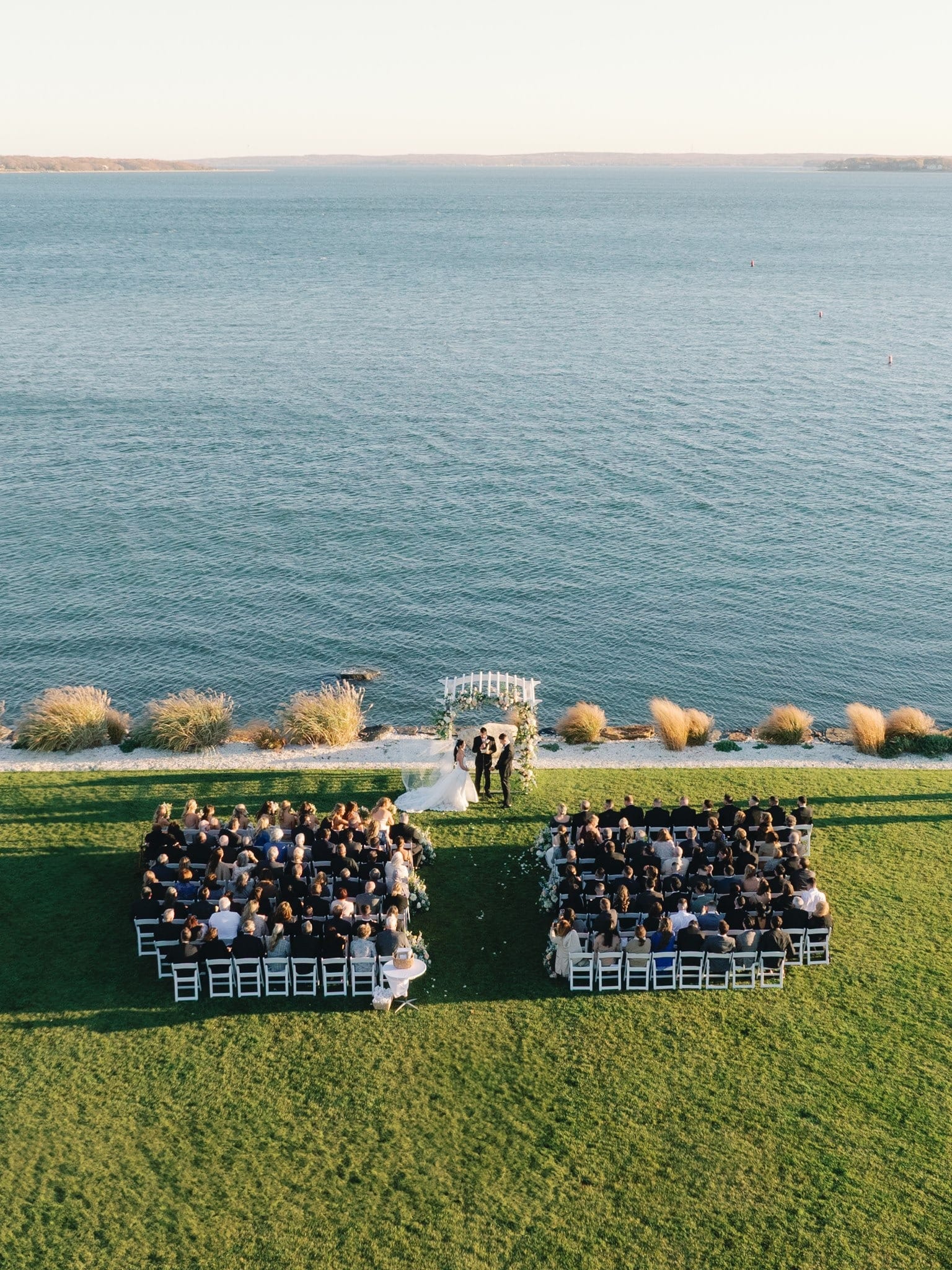 Aerial view of a lakeside ceremony with guests seated on the lawn