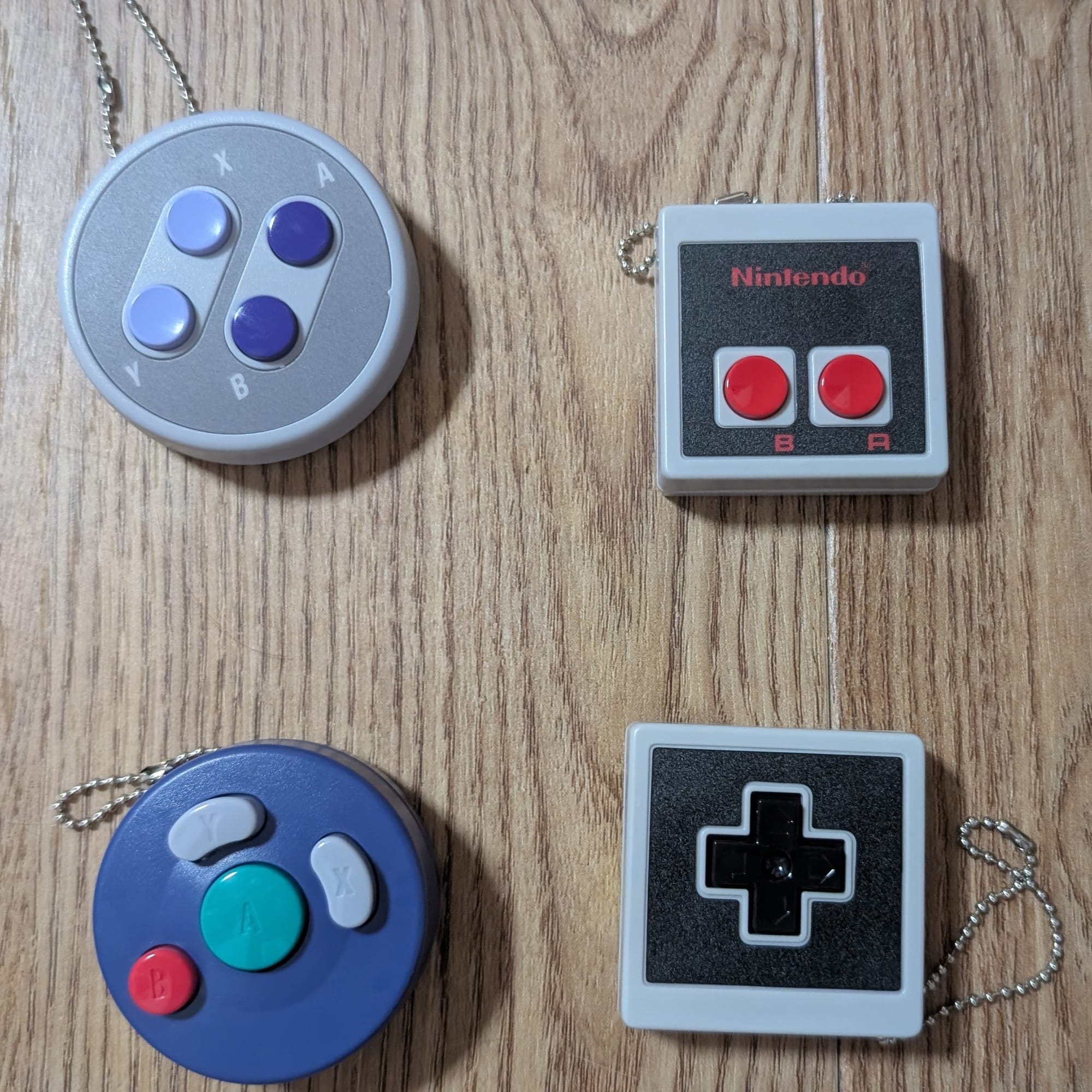 (Top left) a keychain of the face buttons from a North American SNES controller, (top right) a keychain of the face buttons from the North American NES controller, (bottom left) a keychain of the face buttons of the Gamecube controller, (bottom right) a keychain of the D-Pad from the North American NES controller.