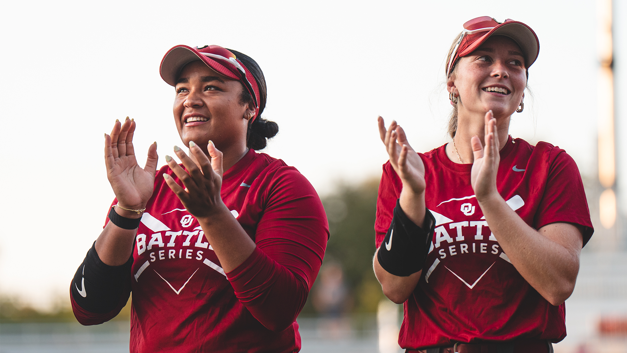 Two Oklahoma players in Battle Series jerseys applaud from the dugout