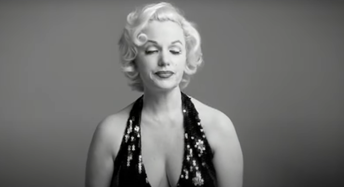 Black and white photo of a blonde Marilyn Monroe lookalike wearing a disdainful expression and dark, sequined gown with a deep plunge neckline