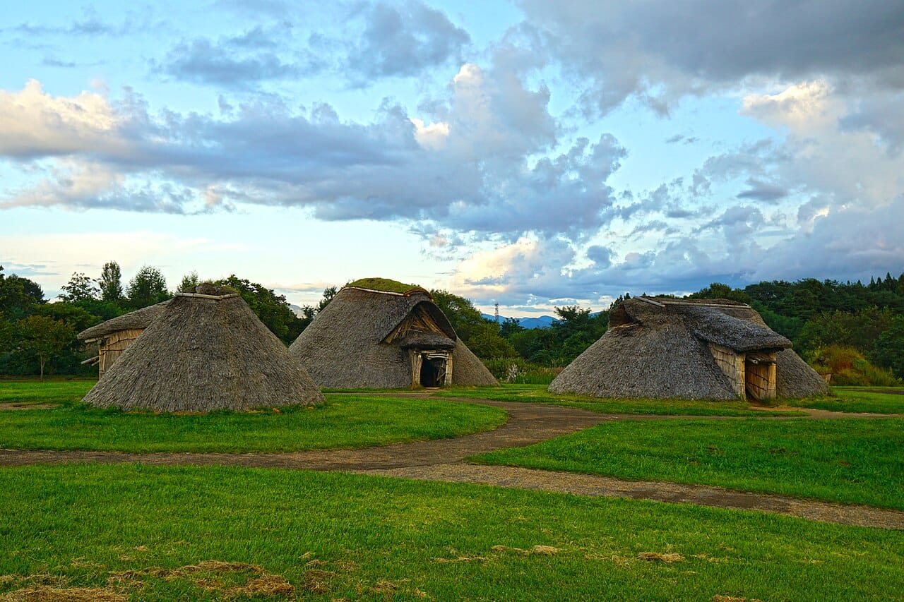 Ancient houses with thatch roofs on a grassy area with blue sky and clouds