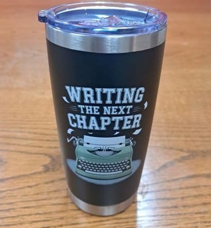 A tumbler with a picture of a typewriter and words "Writing the Next Chapter"