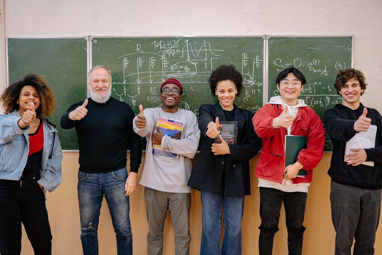 Photo of a professor and his students smiling and holding thumbs up