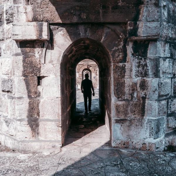 Photo of a man walking in a narrow tunnel in stone ruins