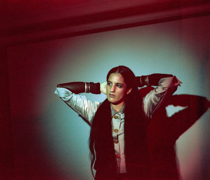 A picture of the artist Ami Dang in a grey button-up shirt, holding the back of her hair and looking off to one side.