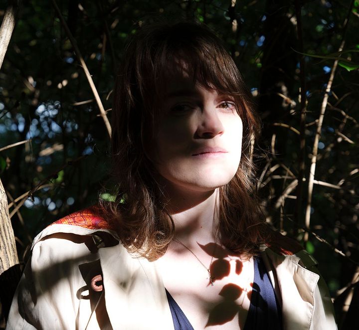 A picture of the artist Haela Ravenna Hunt-Hendrix by Alexander Perrelli, in amongst the branches of trees.