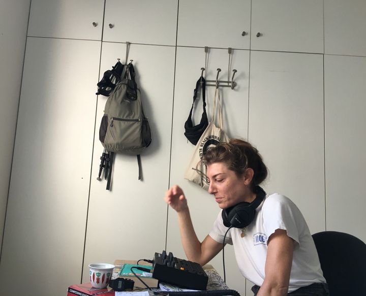 A picture of Bana with headphones around her neck, sat in front of a sequencer.