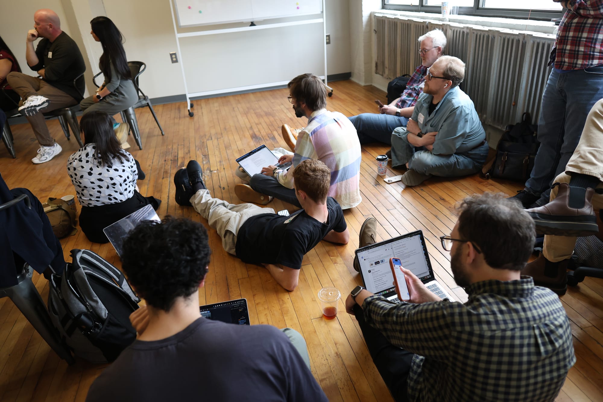 Attendees at the Hacks/Hackers AI x Journalism Summit 2026 sitting and lying on the wooden floor of The Real News Network warehouse with their laptops