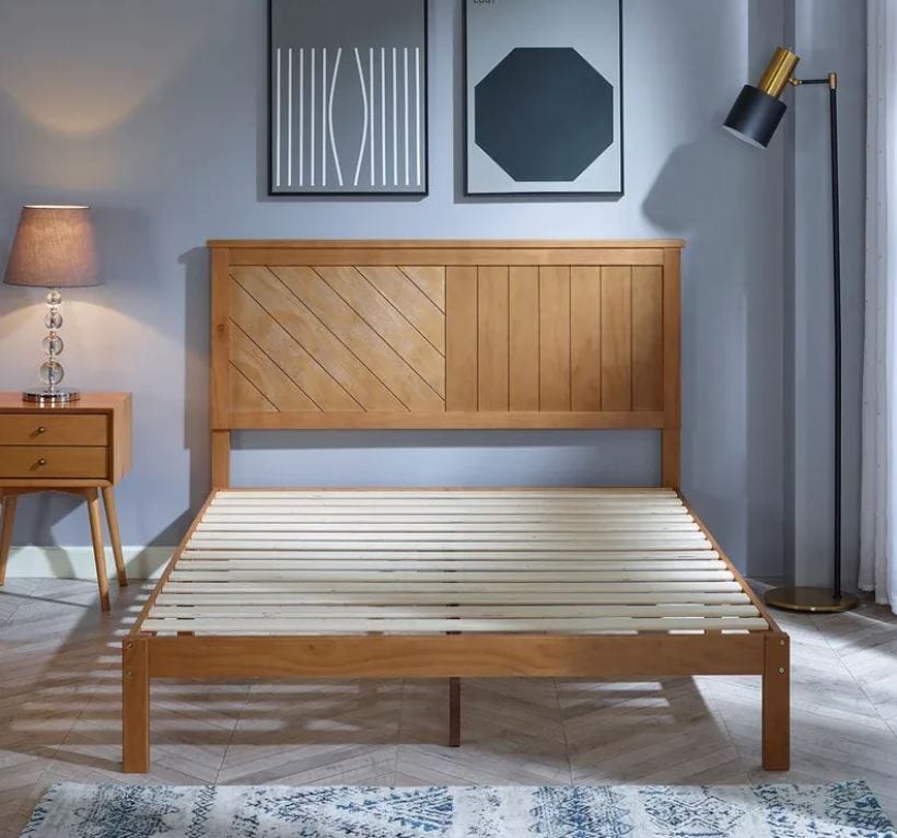 solid pine wood queen platform bed with a contemporary headboard; rustic bed for farmhouse style bedroom; blue walls with geometric art and a blue and white throw rug on the floor; midcentury modern nightstand with modern lamp in the corner of the room