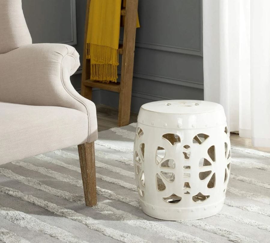 Walmart garden accents for sale; ceramic stool with floral cutouts next to off-white accent chair on a white striped rug with a wooden accent ladder in the corner of the room; Michael's garden accent stool for sale