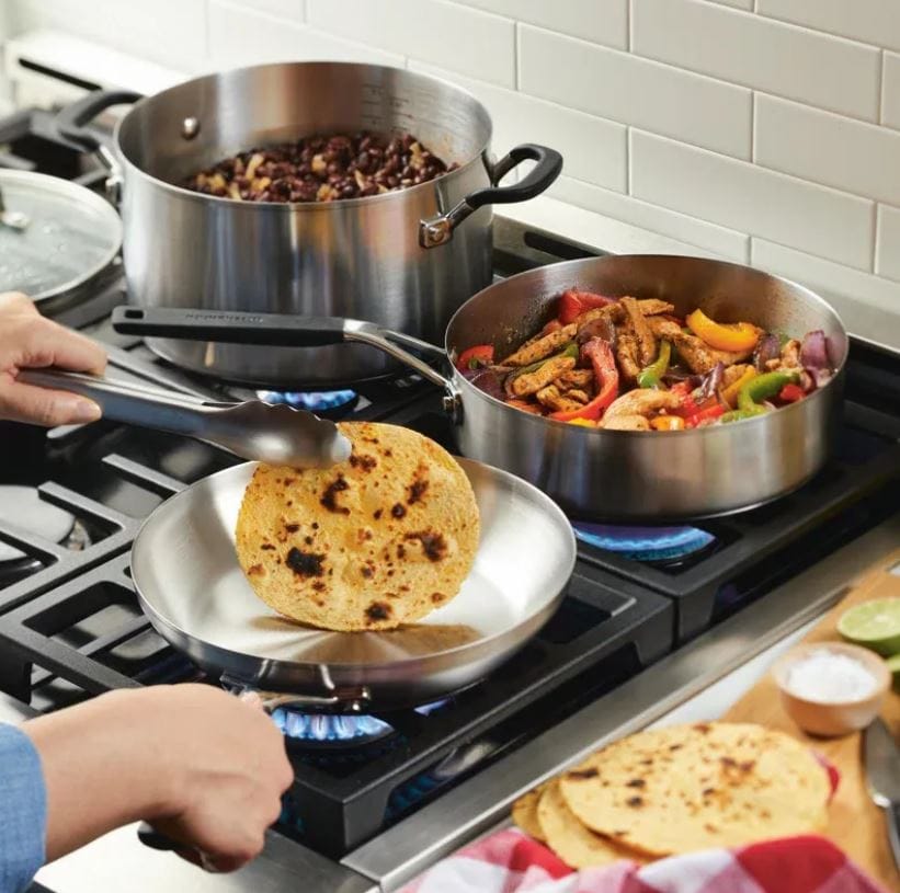 stainless steel Kitchen Aid cookware; stainless steel cookware on the stove with tortillas and fajita toppings