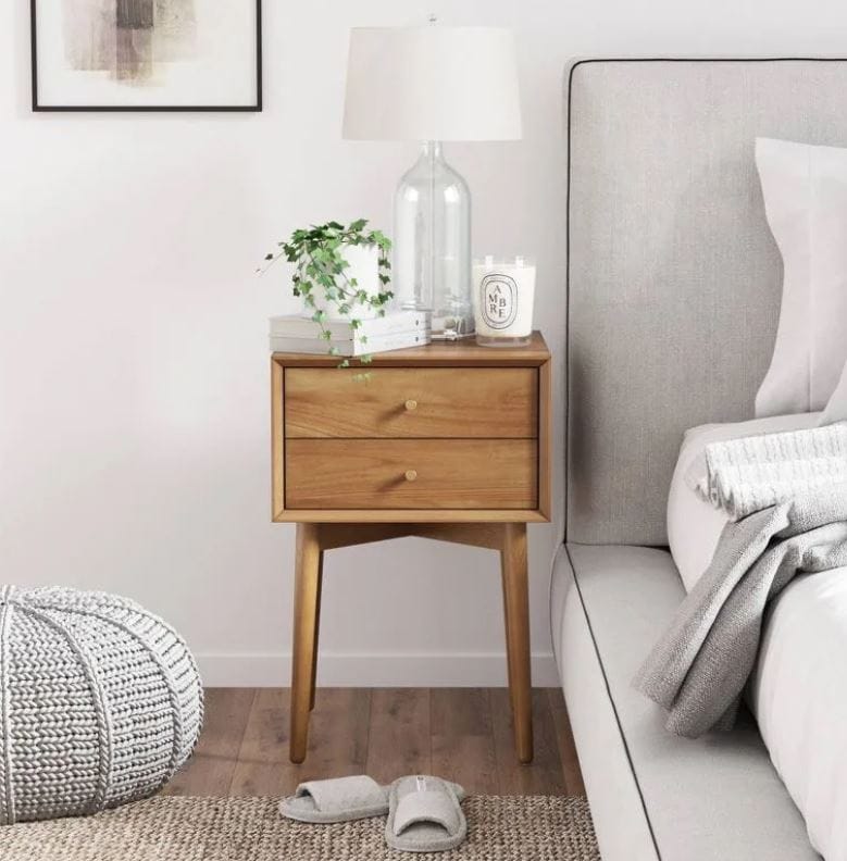 midcentury nightstand with tapered legs; aliexpress nightstand with two drawers; aesthetic oak wood nightstand beside upholstered bed, cream colored pouf on the floor, and slippers beside the bed