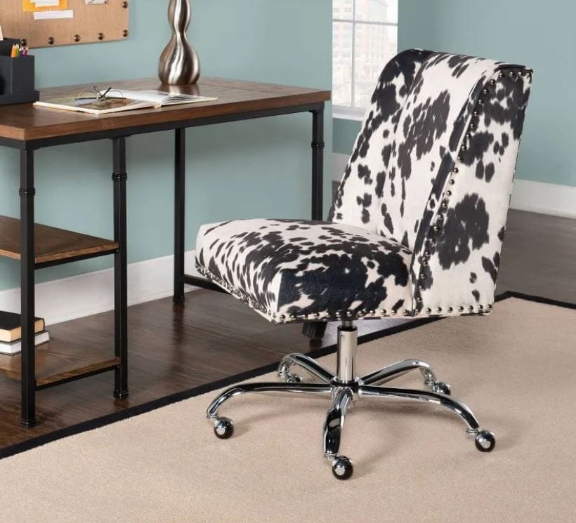 Urban Outfitters furniture for the home office; cow print desk chair next to wooden writing desk on a beige carpet in a room with blue walls; plush rolling desk chair